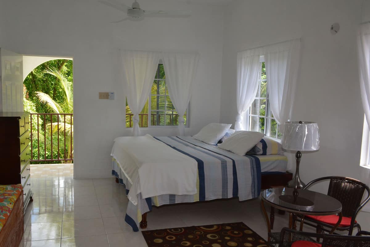 A bedroom with a bed, a desk, a chair, and a view of greenery outside.