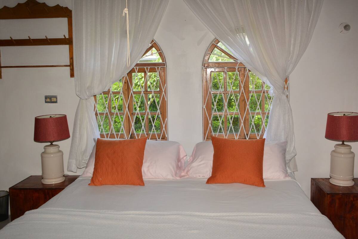 A bedroom with a bed, two nightstands, a window with a wooden lattice, and a curtain.
