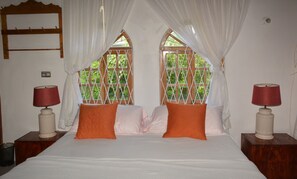 A bedroom with a bed, two nightstands, a window with a wooden lattice, and a curtain. - Cozy Coco (Negril)
