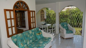 A covered patio area with a sofa and chairs, a small table, and a view through a lattice fence. - Cozy Coco (Negril)