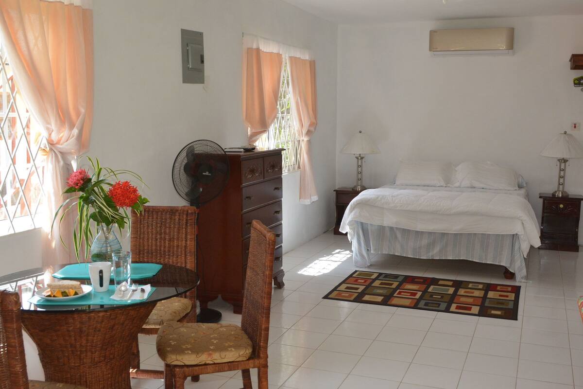 A bedroom with a bed, bedside table, lamp, and a dining area with a table and chairs.