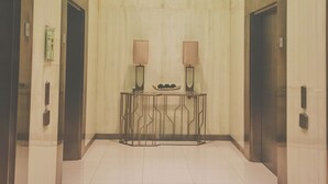 A modern elevator lobby with a glass partition, two lamps on a console table, and a clean tiled floor. - Vista Shaw by Charles (Mandaluyong)