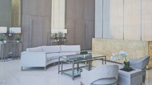 A modern lobby with a white sofa, a glass coffee table, and a seating area with chairs. - Vista Shaw by Charles (Mandaluyong)