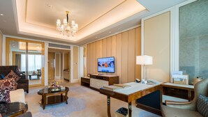 A spacious hotel room with a large flat-screen TV, a desk with a lamp, a comfortable sofa, and a decorative coffee table.