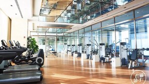 A modern gym with cardio machines, weight stations, and a wooden floor.