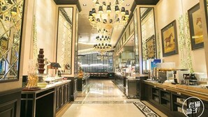 A luxurious hotel lobby with a grand chandelier, a long reception desk, and framed artwork on the walls.