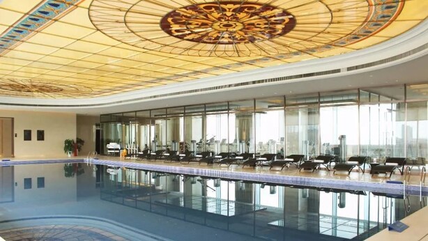 A large indoor swimming pool with a glass wall on one side and a decorative ceiling.