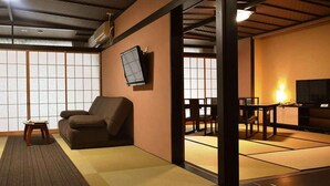 A traditional Japanese room with tatami flooring, a low table with a chair, a sofa, a television mounted on the wall, and sliding doors. - Tokiwa Hotel (Nasushiobara)