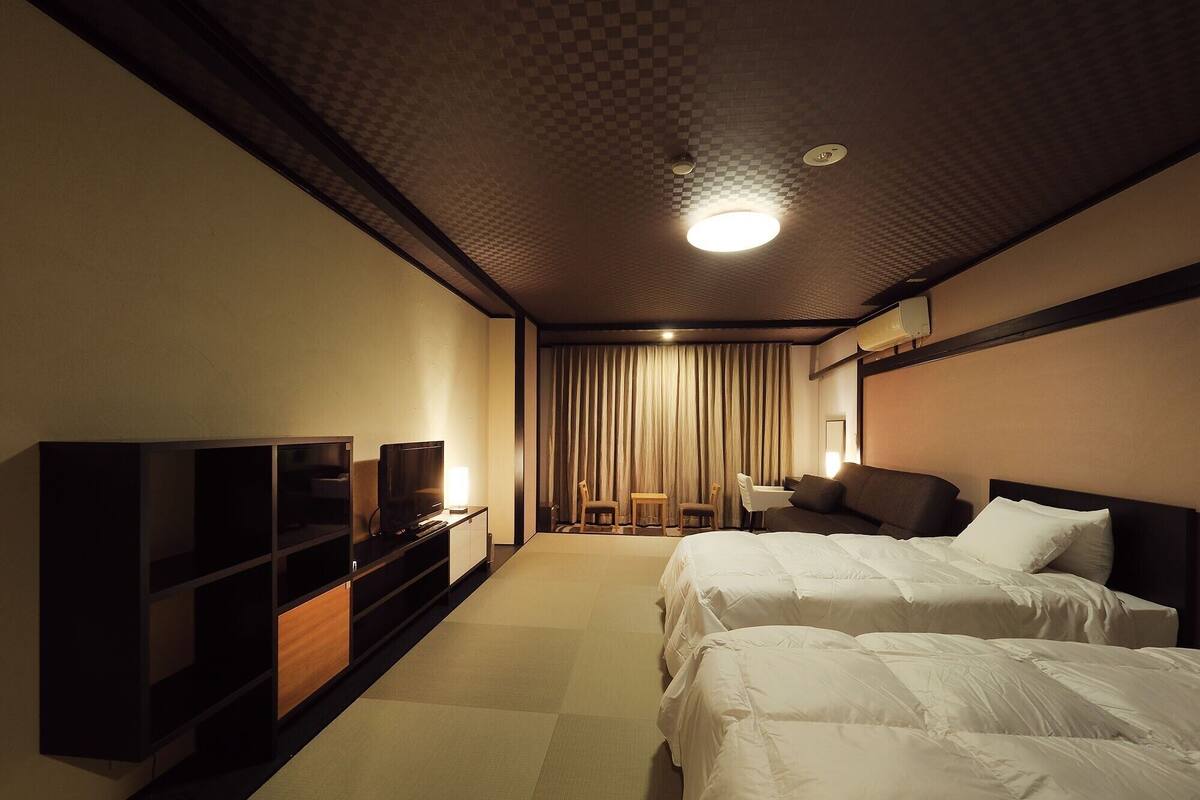 A hotel room with two beds, a TV, a desk, and a chair.