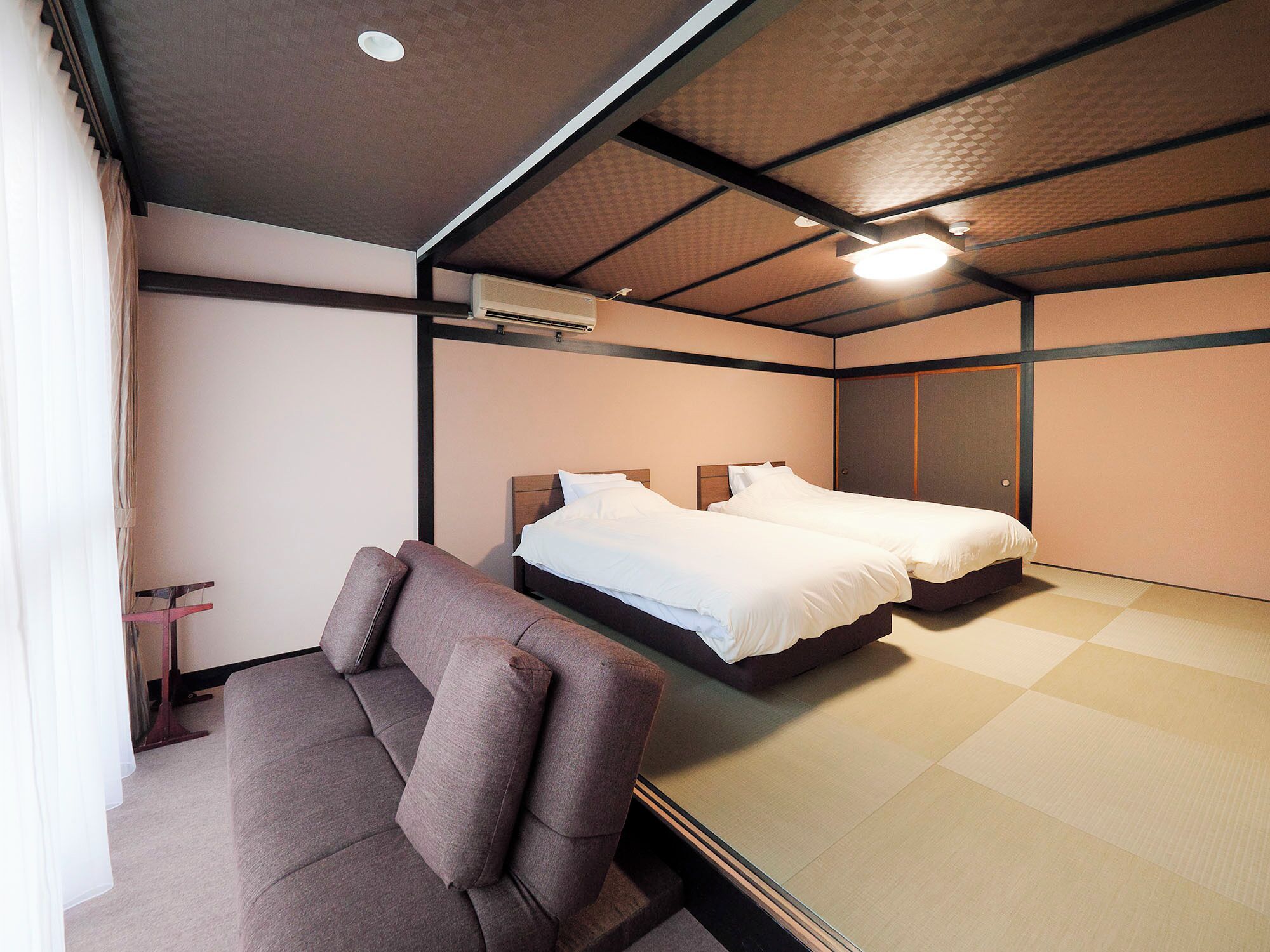A hotel room with two beds, a sofa, a ceiling fan, and a large mirror.