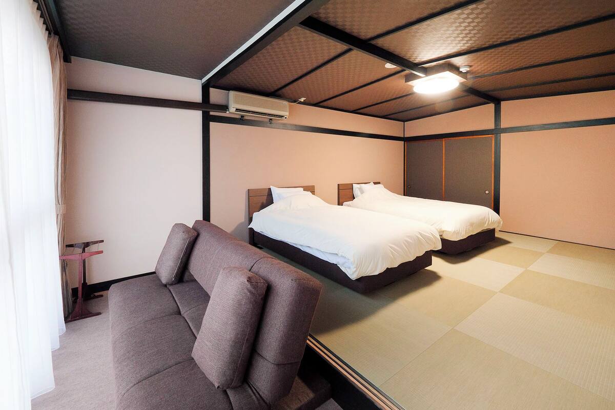 A hotel room with two beds, a sofa, a ceiling fan, and a large mirror.
