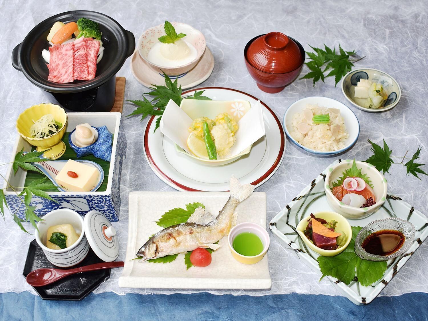Verschiedene japanische Gerichte, darunter rohes Fischfilet, Reis und Gemüse, sind auf einem Tisch angerichtet.