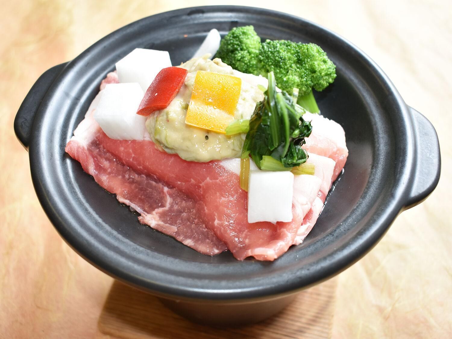 A black bowl containing raw meat, vegetables, and a yellow-orange vegetable.