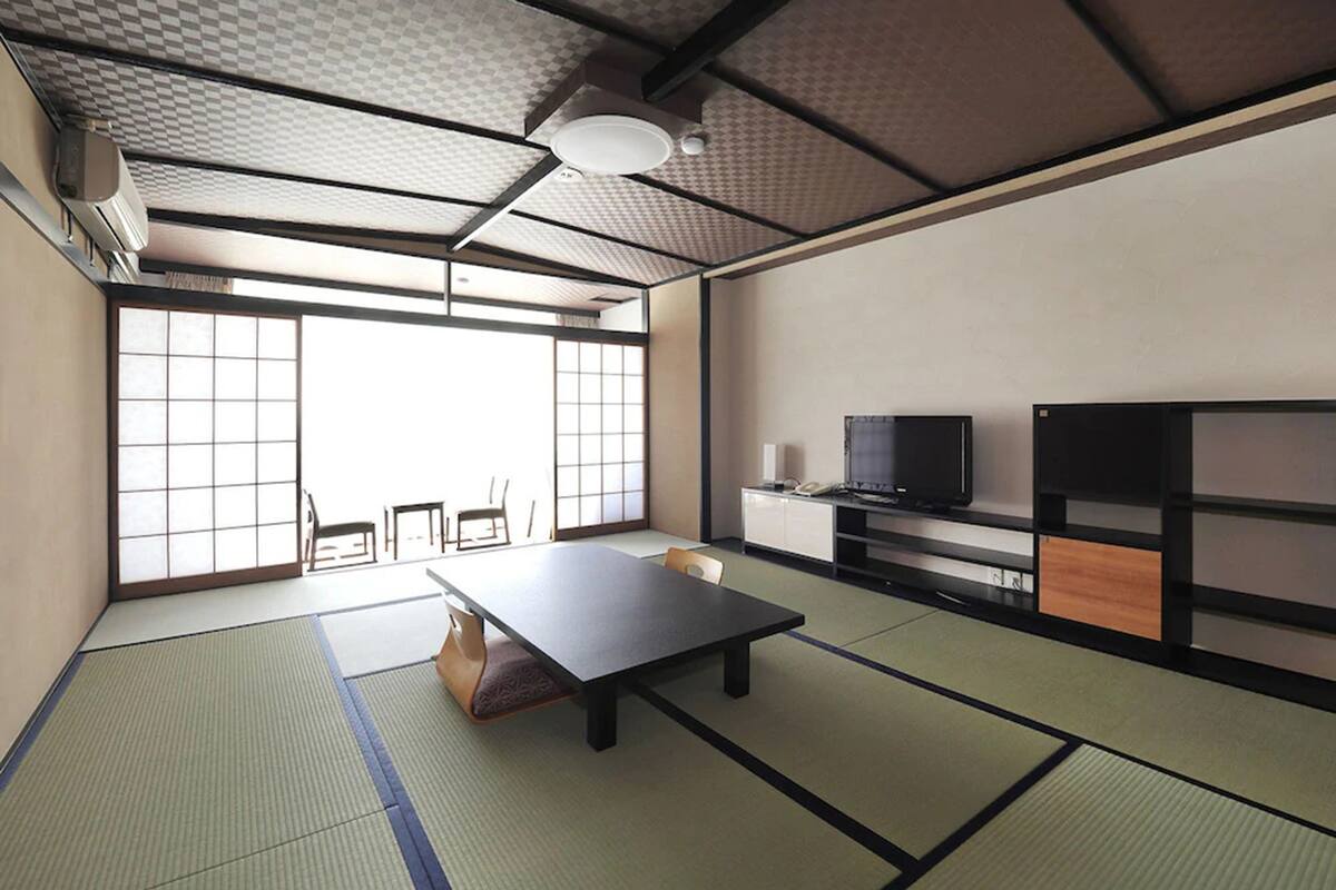 A tatami mat room with a low table, chairs, a TV, and a sliding door.
