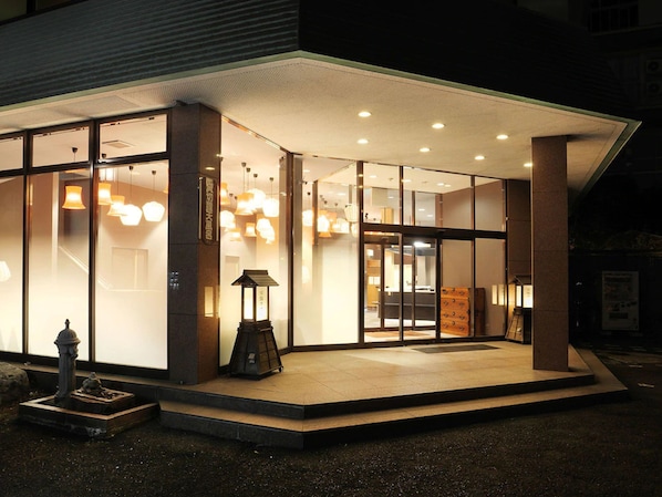 A modern building with large glass windows, a covered entrance, and a small outdoor seating area.