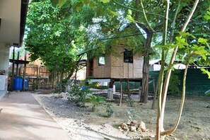 A house with a bamboo structure, surrounded by trees and a gravel path. - Alimpay Foresters Apartment (Panglao)