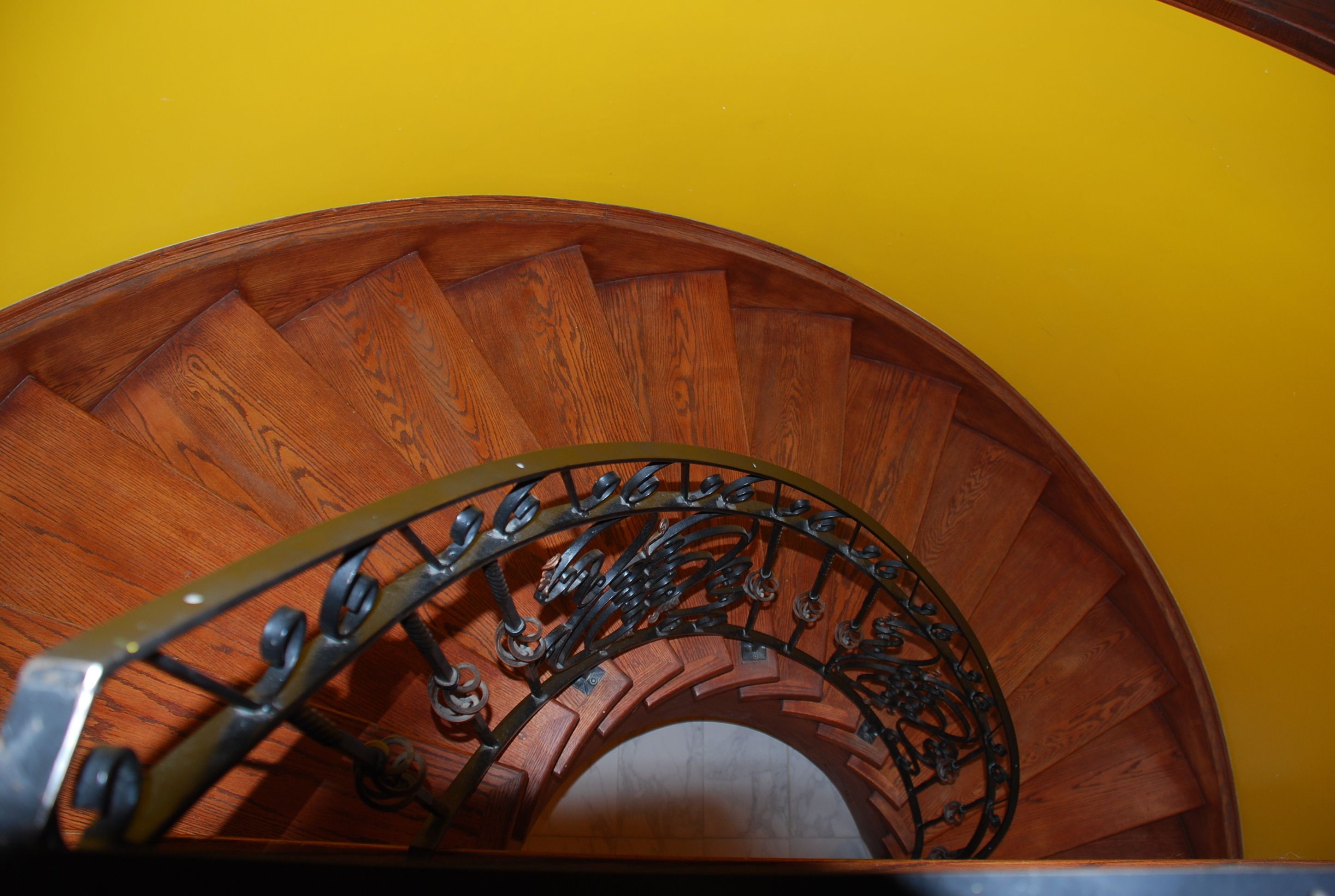 A wooden spiral staircase with a metal railing against a yellow wall.