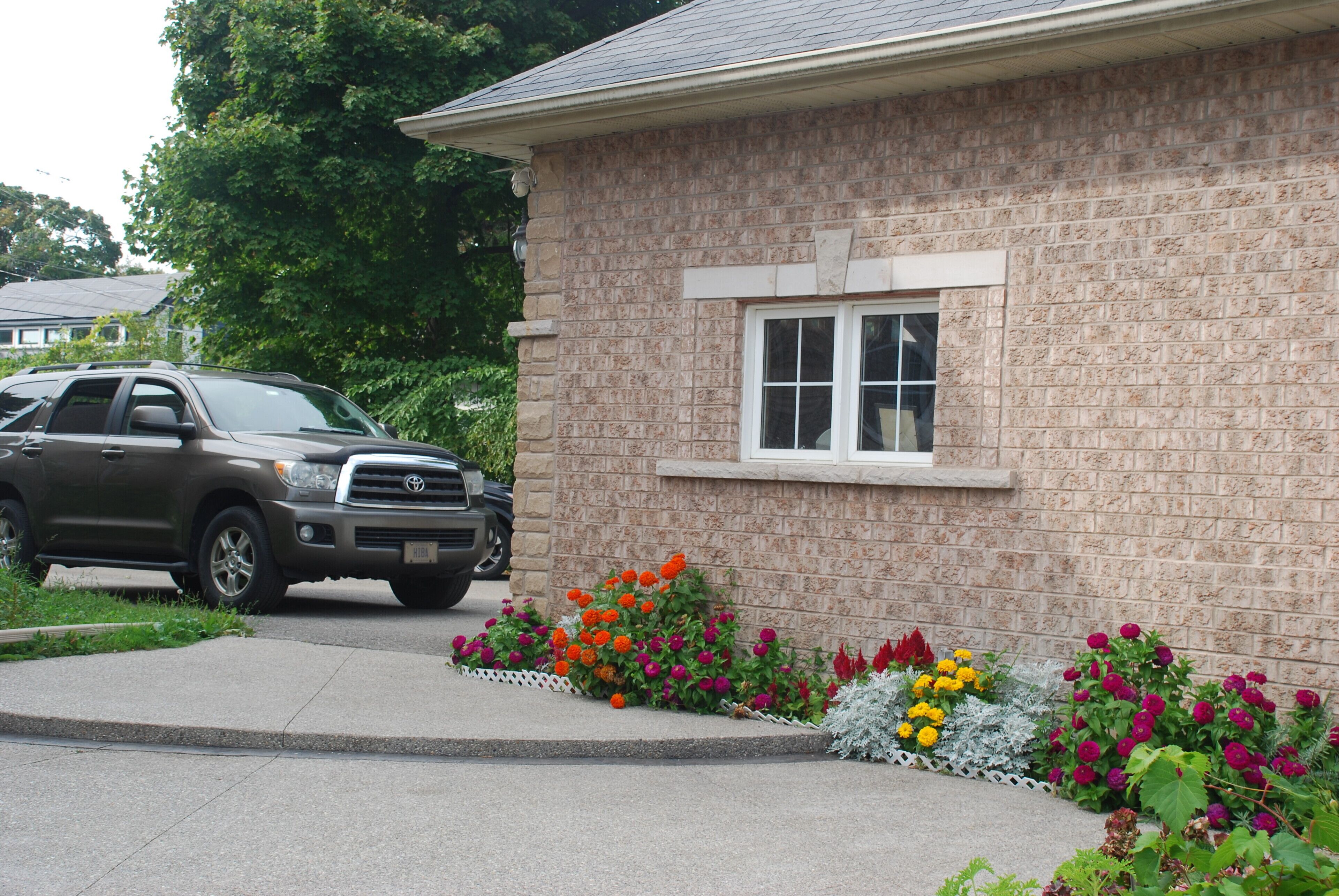 A house with a brick exterior, a driveway, and a garden with various flowers.