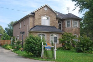 A two-story house with a stone facade, a front porch, and a gated entrance. - Malak Bnb (Fort Erie)