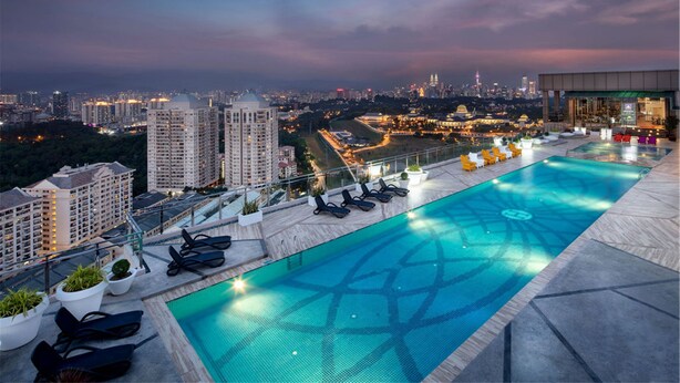 Una piscina infinita en la azotea con vistas a la ciudad, sillas de descanso y plantas en macetas.