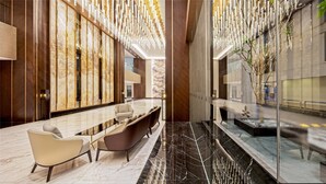 Un vestíbulo moderno con suelo de mármol, un mostrador de recepción, zona de estar y una pared decorativa con luces colgantes.
