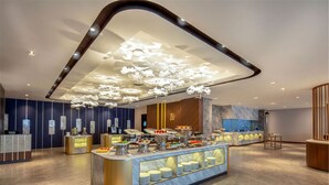 Un lobby moderno de hotel con un área de buffet central, una recepción y una gran pared de mármol.