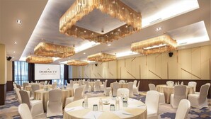 Un salón de conferencias con mesas redondas, sillas blancas y candelabros colgantes.