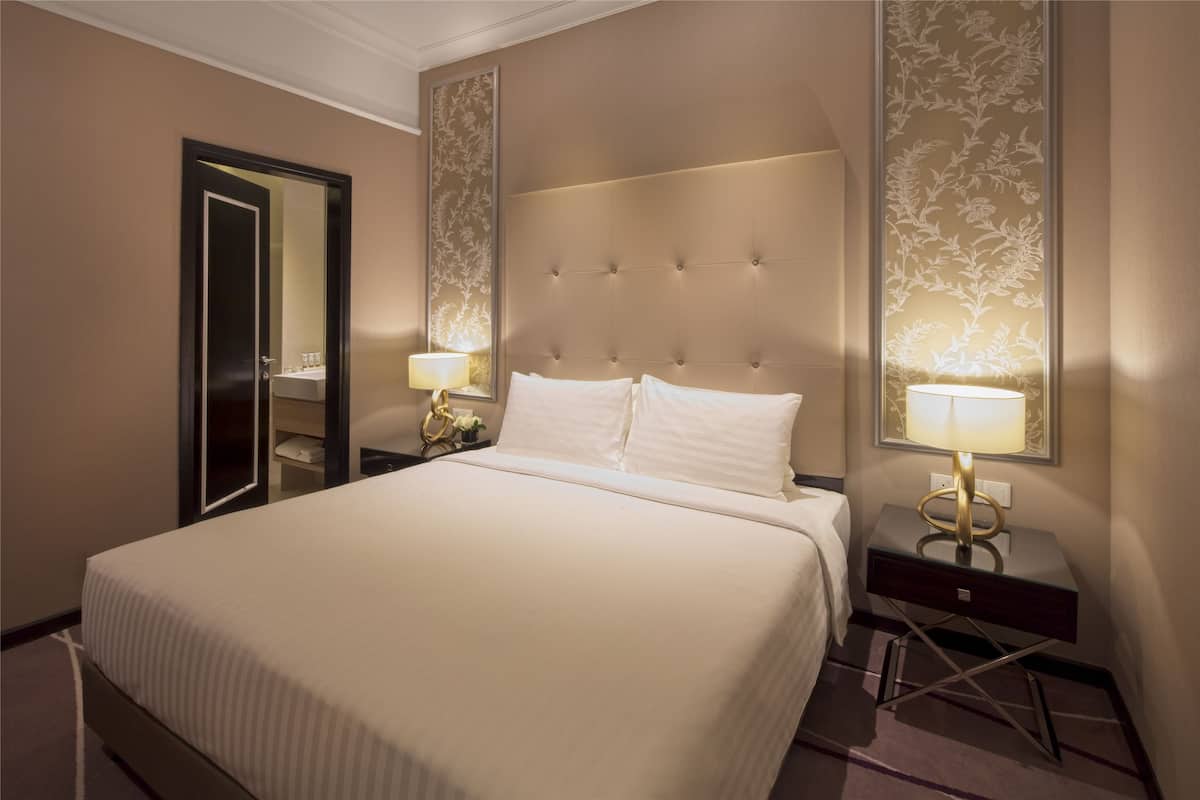 Hotellihuone, jossa on suuri sänky, kaksi yöpöytää valaisimineen, peili ja koristeellinen seinäpaneeli.