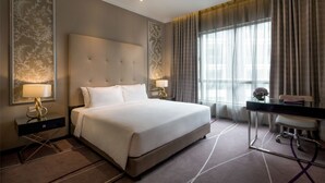Habitación de hotel con una cama grande, dos mesitas de noche con lámparas, un escritorio con silla y un ventanal con cortinas.