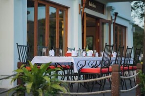 An outdoor dining area with tables set for two, chairs, and a rope barrier. - Le Grand Pakbeng (Oudomxay)