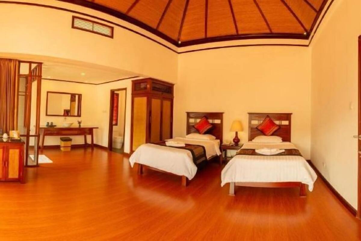 Ein Hotelzimmer mit zwei Betten, Holzboden, gewölbter Decke und einem Spiegel an der Wand.