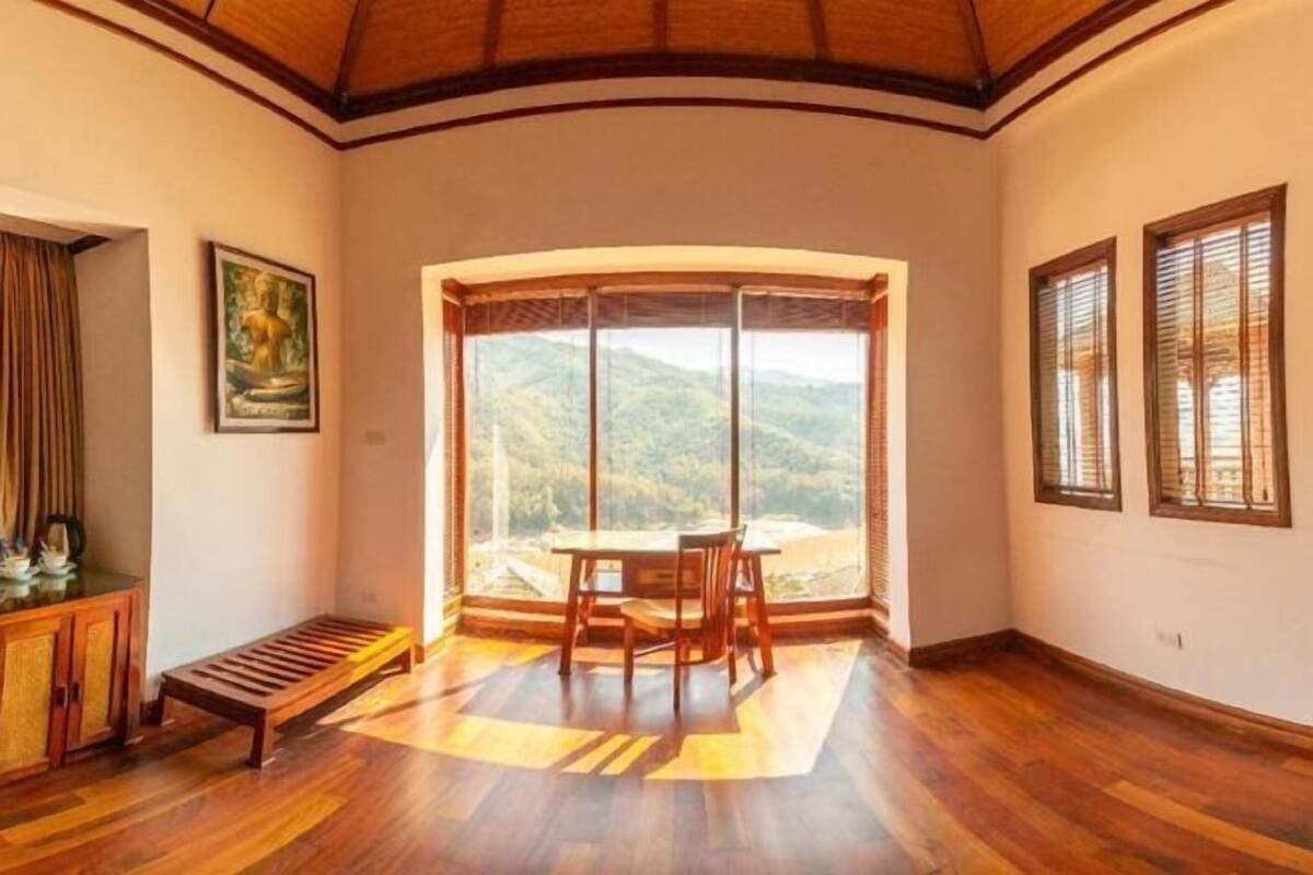 Ein Zimmer mit einer Holzbank, einem Tisch mit Stühlen, einem großen Fenster mit Bergblick und einem gerahmten Bild an der Wand.