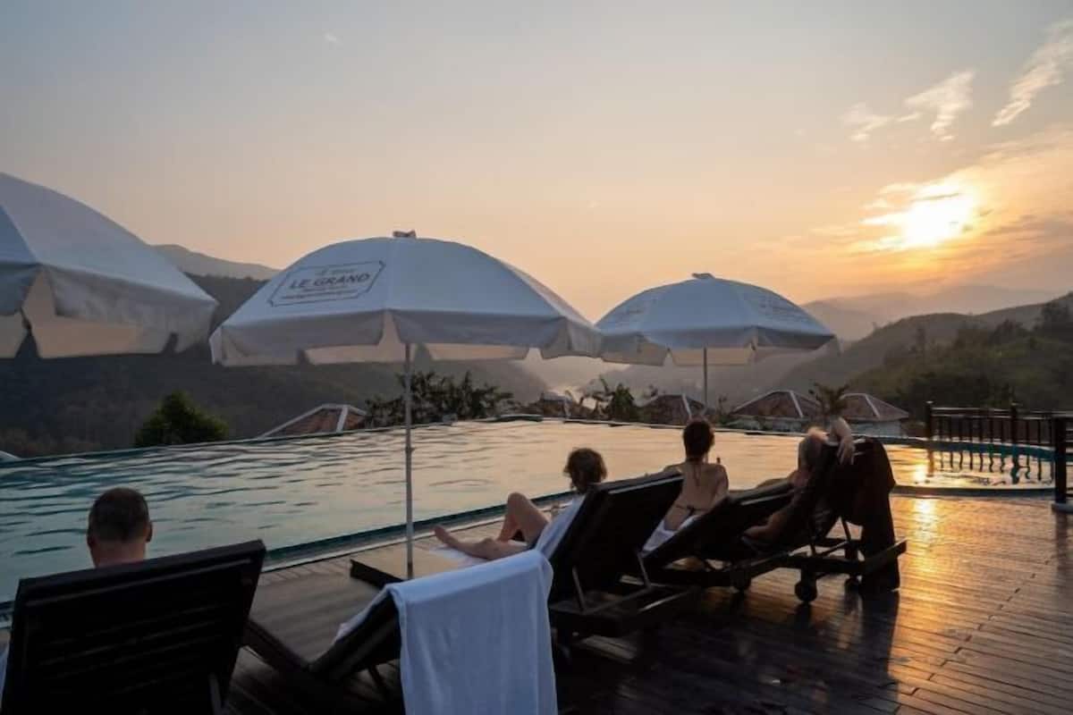 Ein Poolbereich mit Liegestühlen und Sonnenschirmen mit Blick auf einen Pool und Berge.