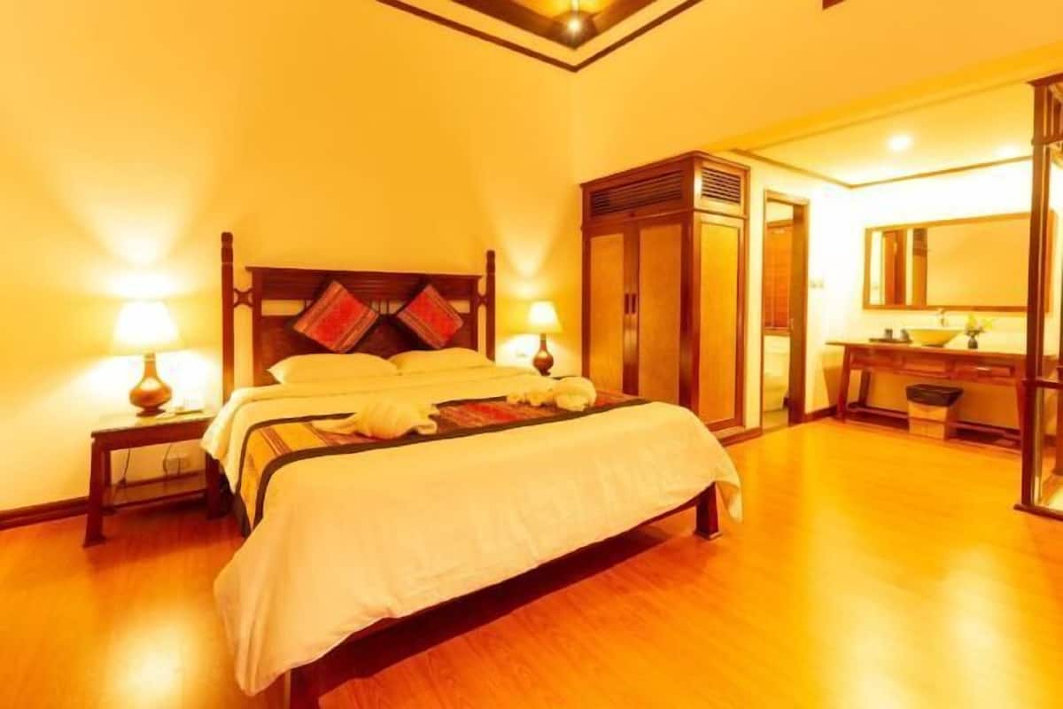 Ein Hotelzimmer mit einem hölzernen Bett, Nachttischlampen, einem Kleiderschrank und einem Badezimmer mit Spiegel und Waschbecken.