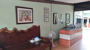 A reception area with a wooden bench, a fan, and a counter with a tiled backsplash. - Baan Plubpla Resort (Chanthaburi)