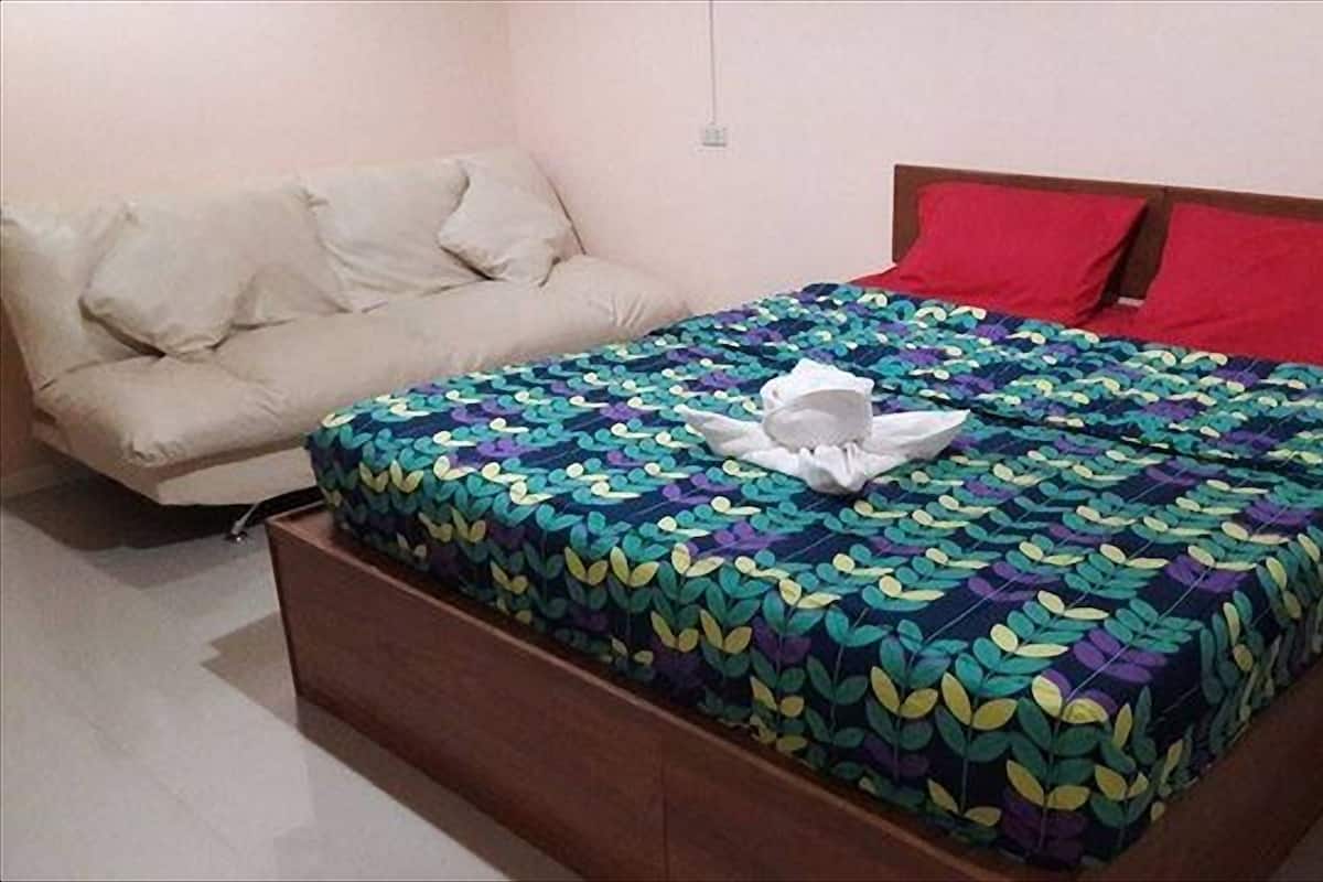 A bed with a colorful leaf-patterned bedspread, a wooden headboard, and two red pillows.