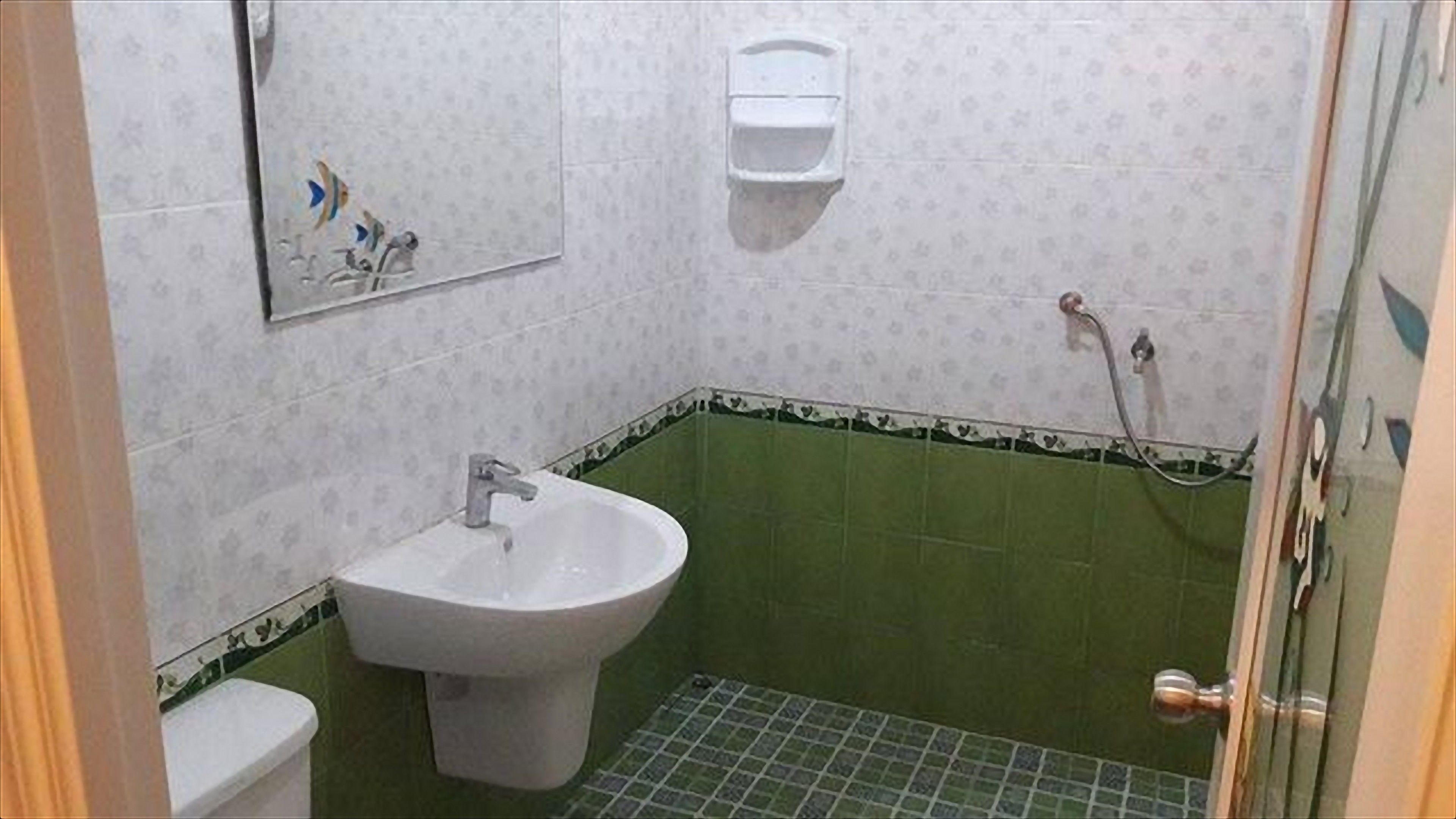 A bathroom with a white sink, a toilet, and a shower area with green tiles.