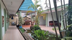 A covered walkway with a small pond, palm trees, and a bench. - Baan Plubpla Resort (Chanthaburi)