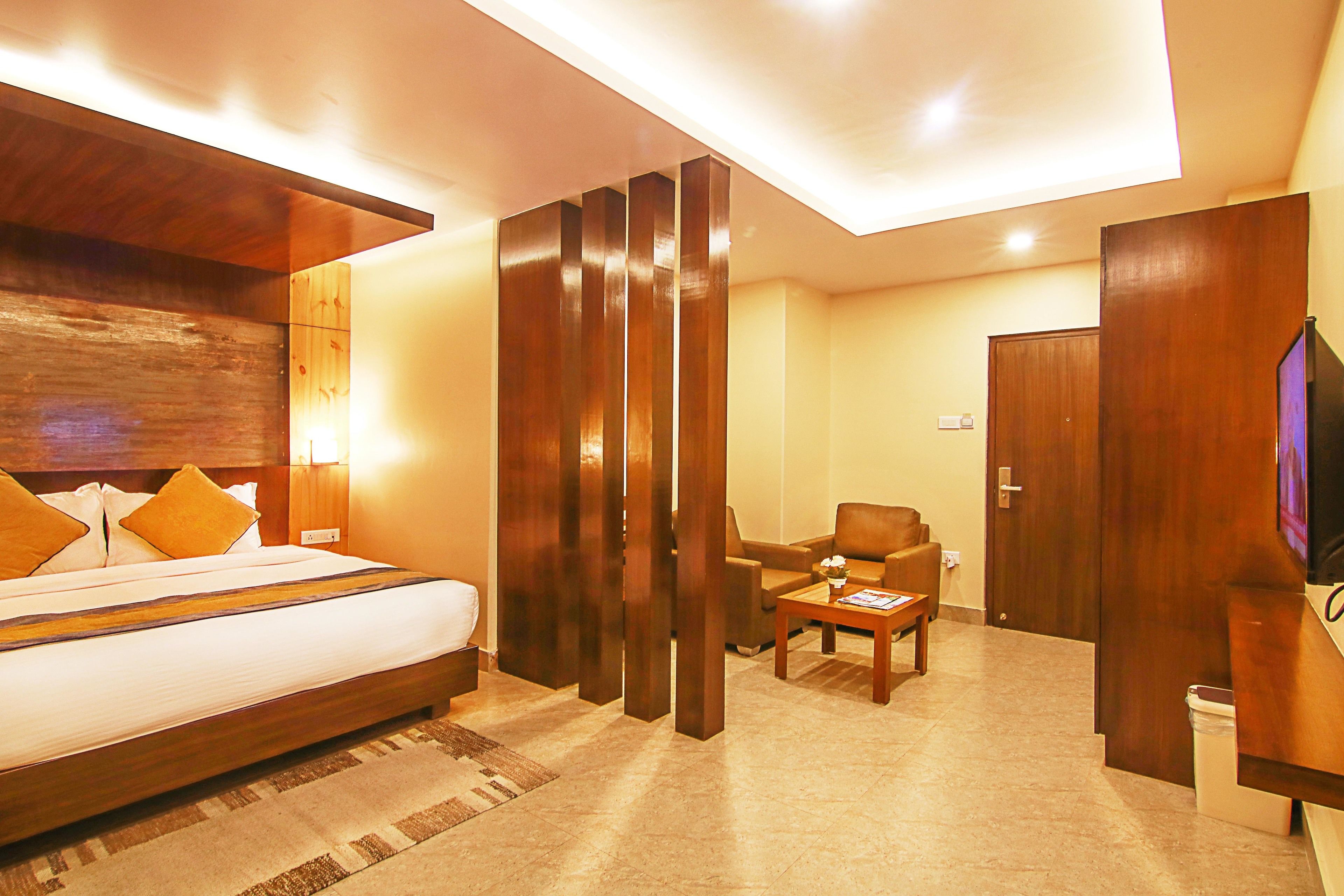 Une chambre d’hôtel avec un grand lit, une tête de lit en bois, un bureau avec une chaise, une télévision et une armoire.