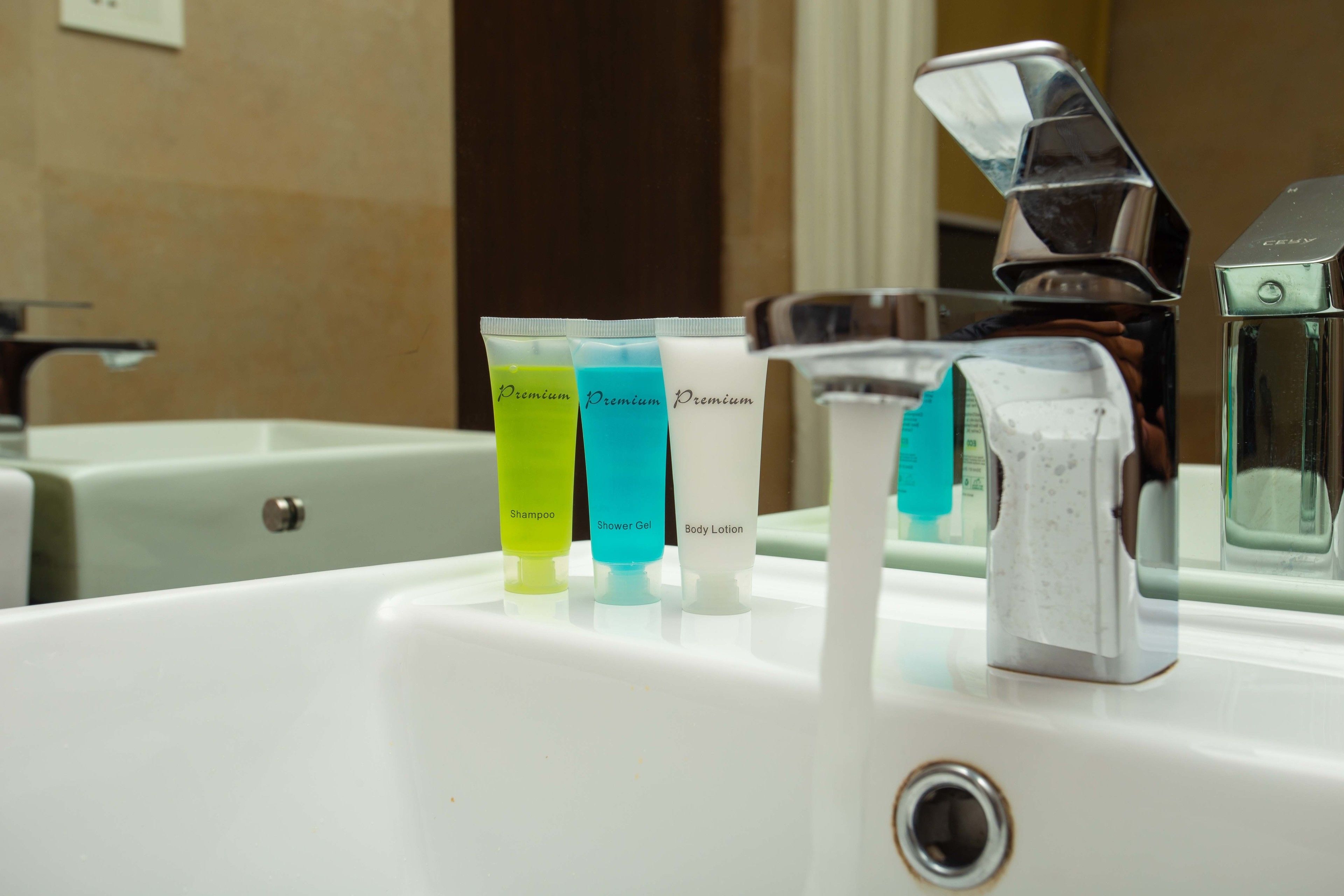 A bathroom sink with three tubes of shampoo, shower gel, and body lotion.