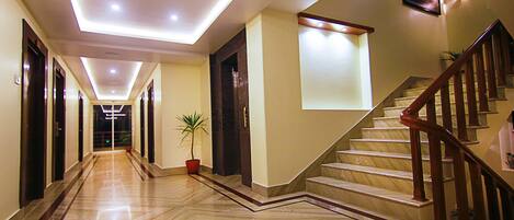 A hotel corridor with a marble floor, a wooden staircase, and a potted plant.