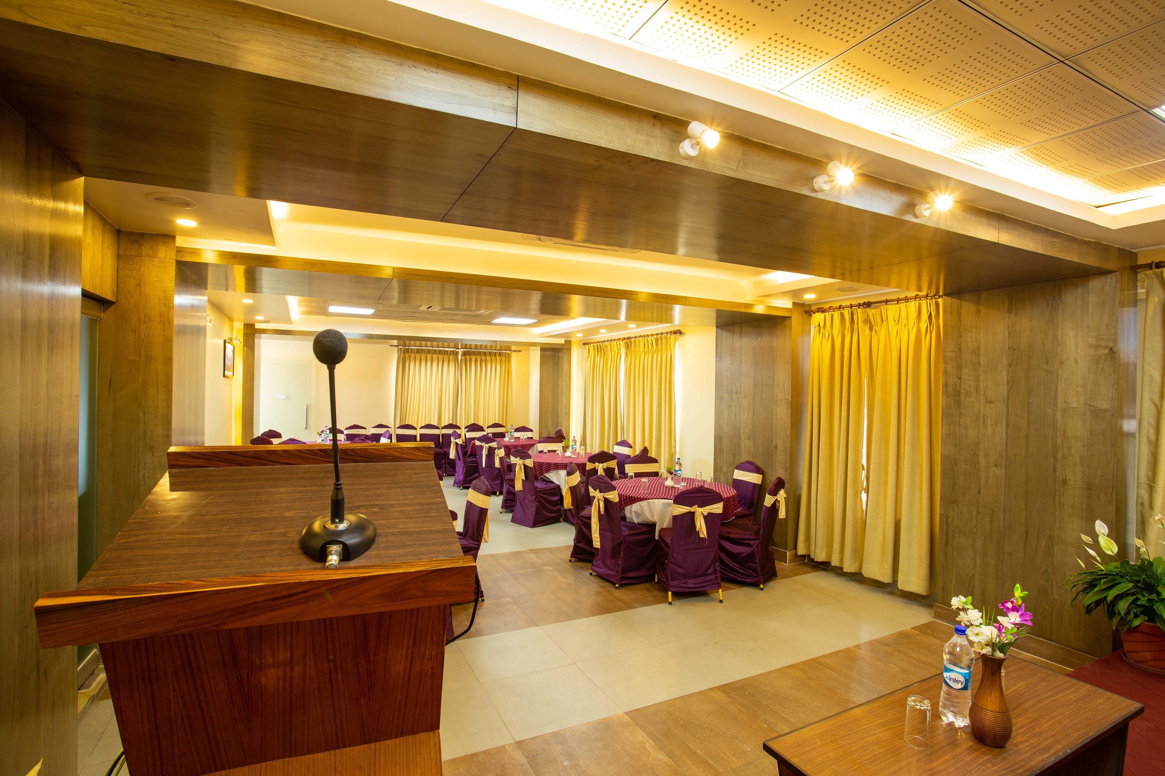 Une salle de conférence avec un pupitre en bois, des tables entourées de chaises violettes et des rideaux jaunes.