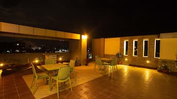 Un'area patio esterna con pavimento piastrellato, sedie di metallo verdi e un tavolo.
