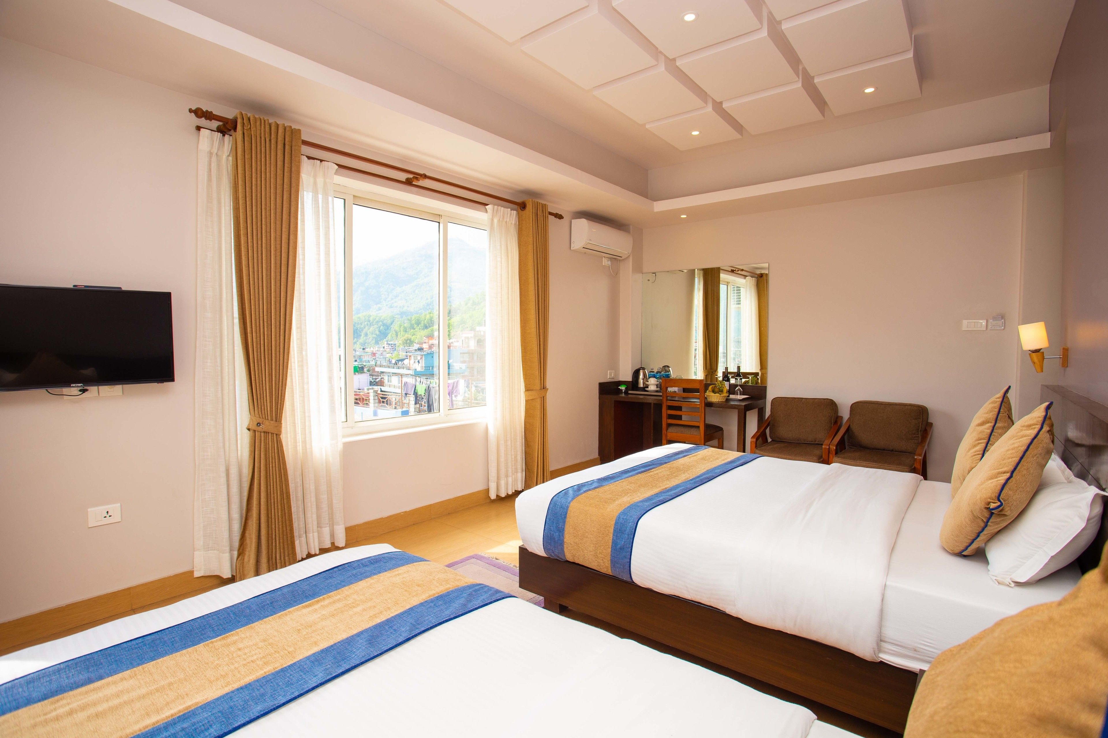 A hotel room with two beds, a desk, a chair, a TV, and a window with curtains.