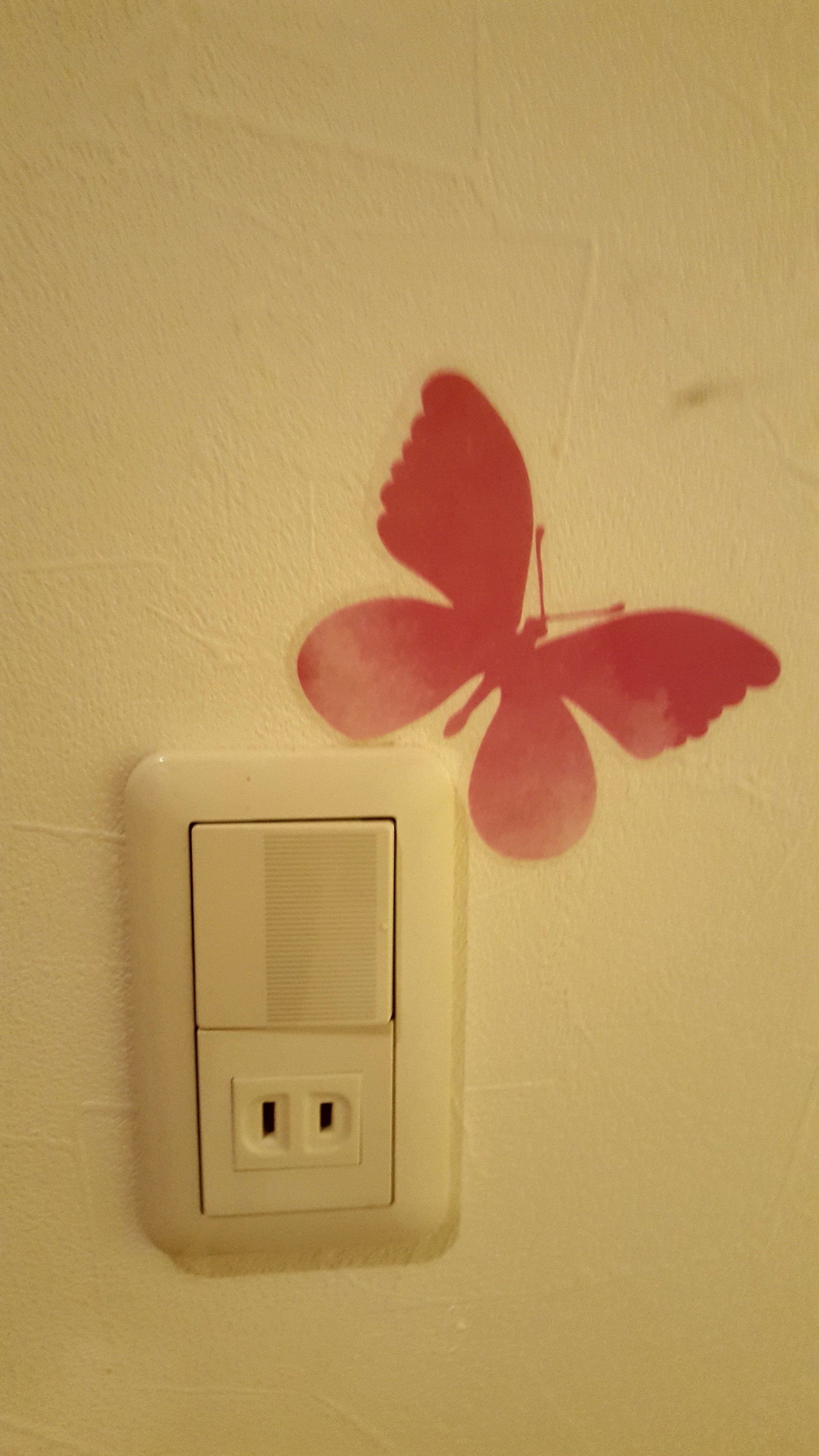 Un enchufe de pared con un adhesivo de una mariposa roja.