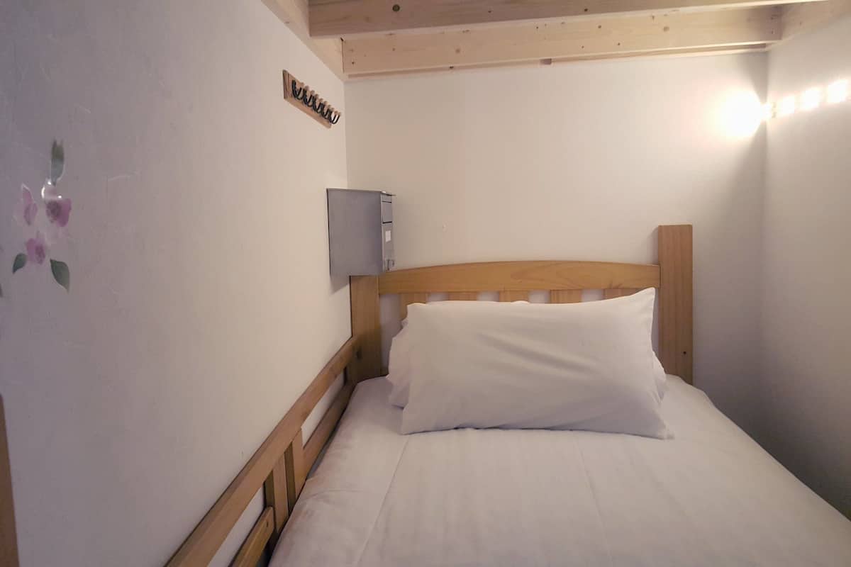 Une petite pièce agréable et chaleureuse, avec un lit en bois, du linge de lit blanc, un radiateur fixé au mur et un élément décoratif mural.