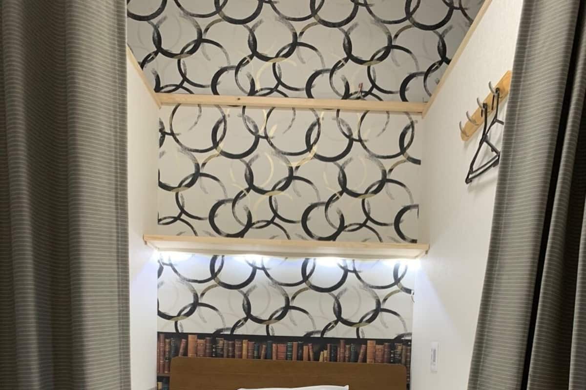 Un lit bien fait, avec du linge de lit blanc et deux serviettes jaunes, une tête de lit en bois et un mur décoré d’un motif.