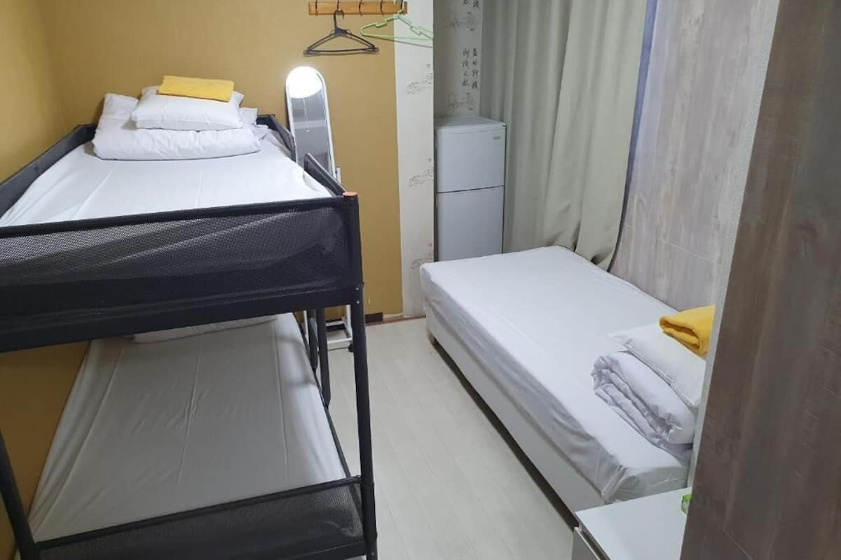 Une petite pièce compacte avec des lits superposés et un lit simple, un petit bureau et un radiateur fixé au mur.