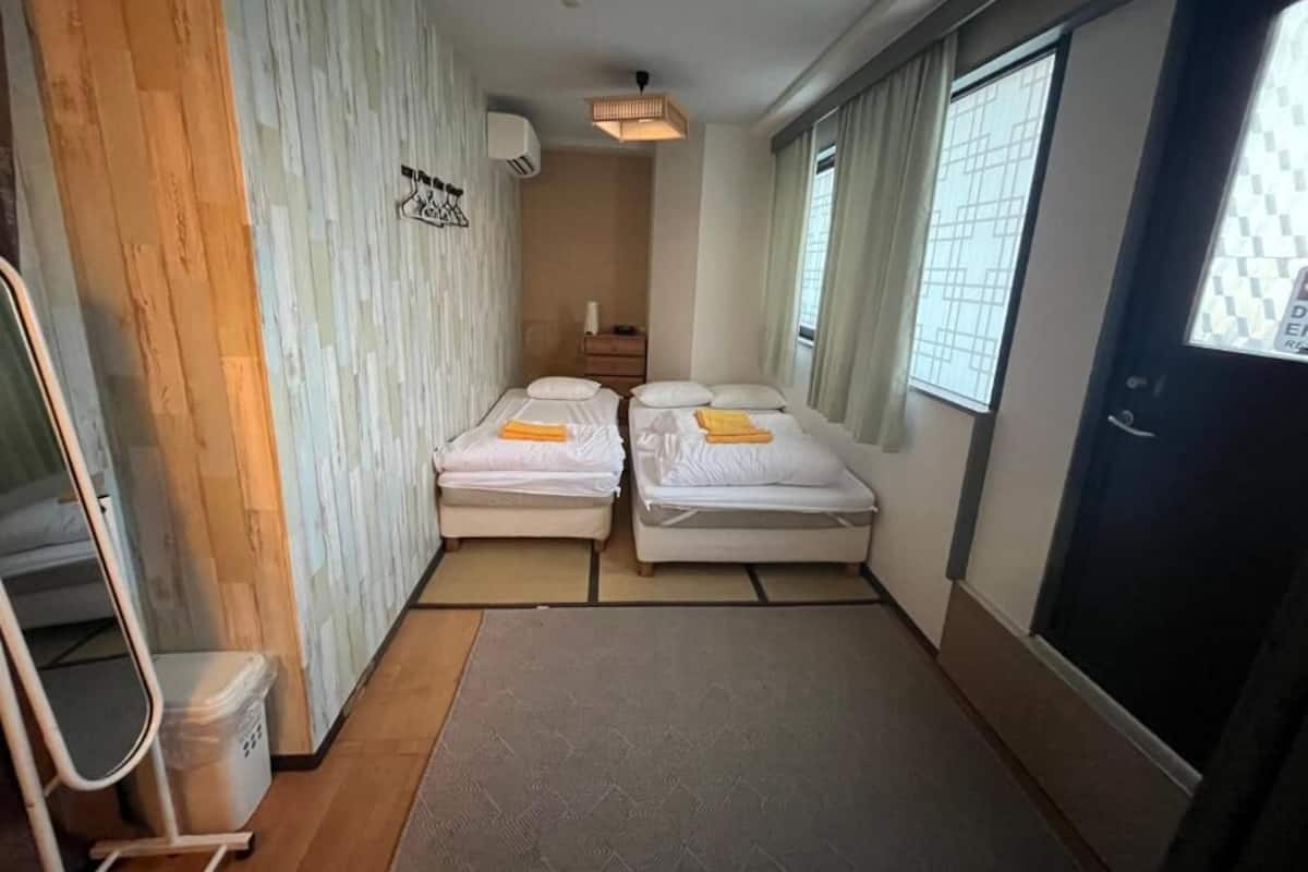 Une chambre d’hôtel de taille modeste, comprenant deux lits simples, une petite table de chevet, un miroir et une armoire.