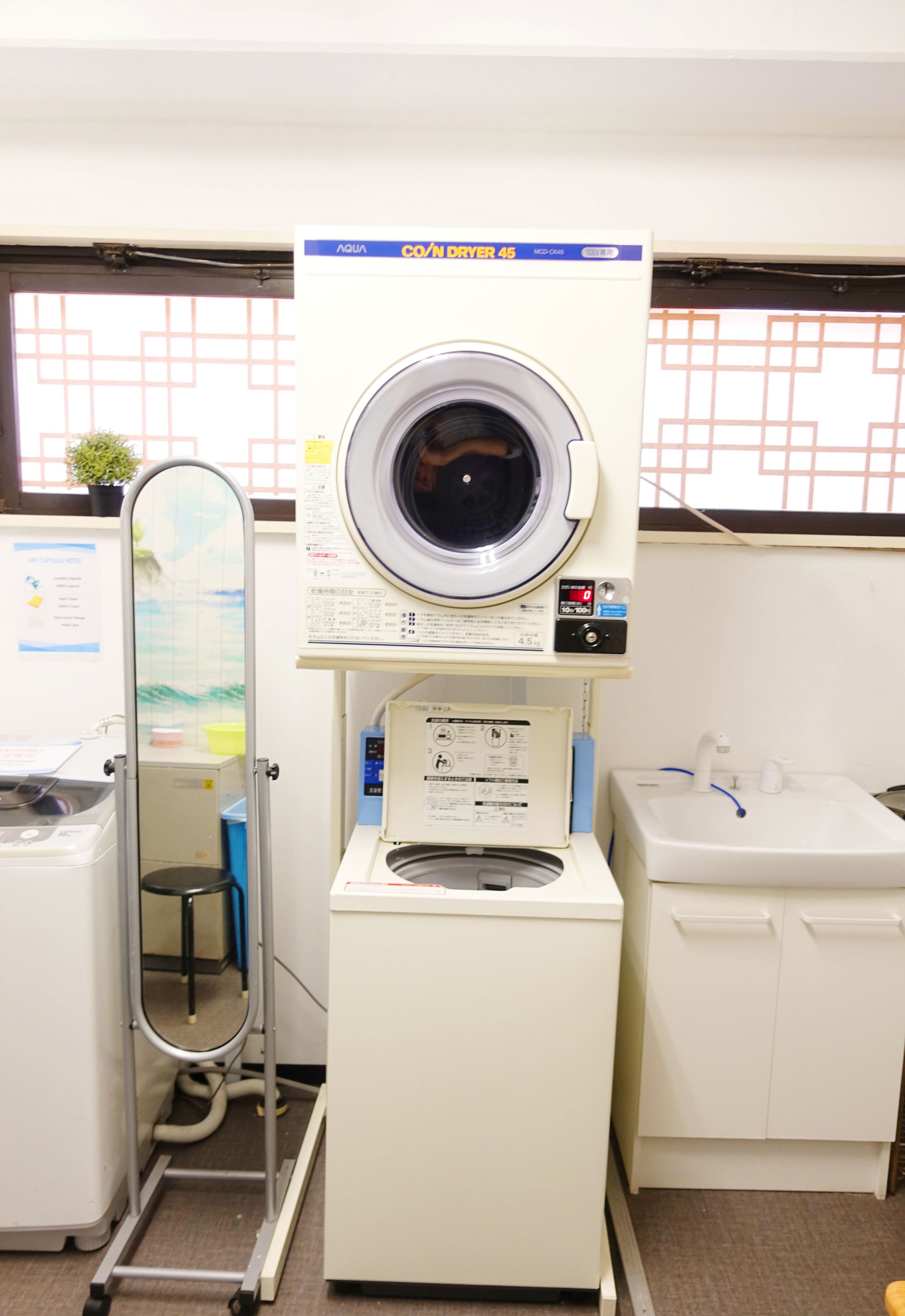 A compact laundry facility with a front-loading washer and dryer, a sink, and a small stool.